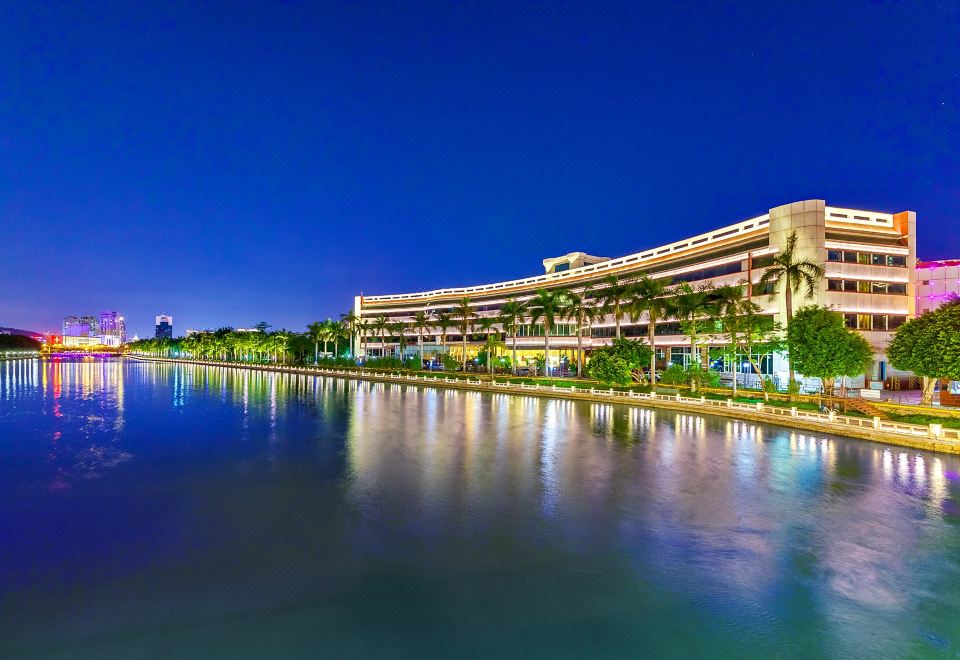 a large building surrounded by water , with palm trees and lights illuminating the area at night at Swan Hotel