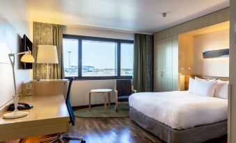 a hotel room with a king - sized bed , a desk , a chair , and a window overlooking the city at Hilton Helsinki Airport