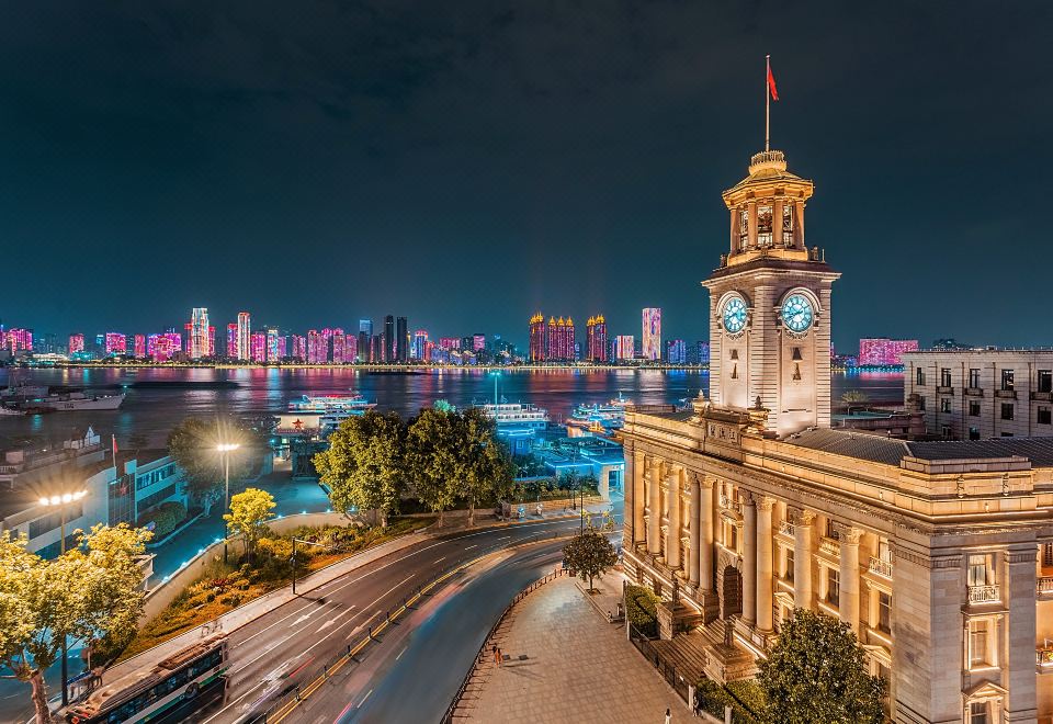 A city at night is depicted with a clock tower and other buildings in the foreground or background at Grand Madison Wuhan Hankou on the Bund