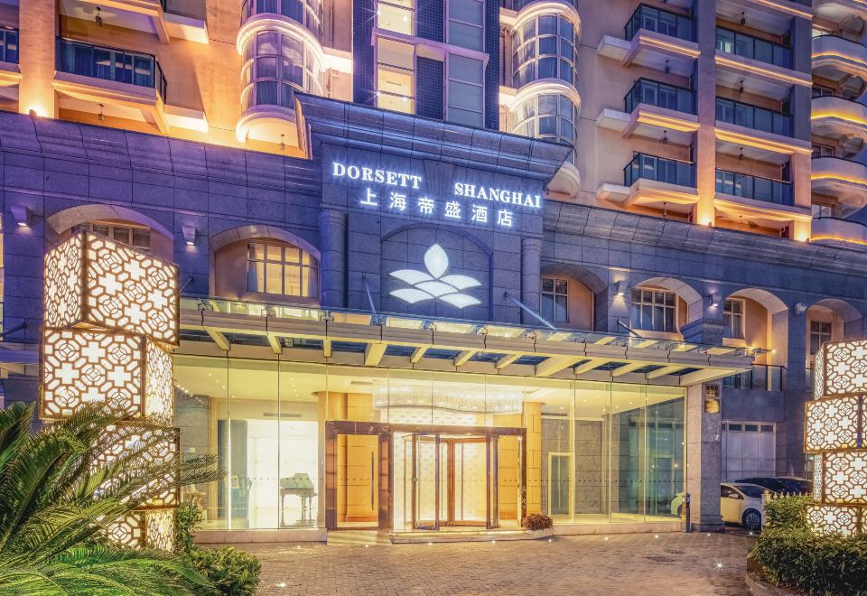 At night, a hotel entrance is adorned with an illuminated sign above its glass door at Dorsett Shanghai
