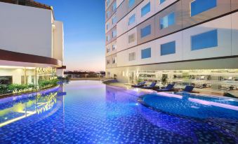 a modern hotel with a large pool and blue lights , surrounded by lounge chairs and a building at Aston Kupang Hotel & Convention Center