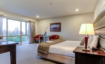 a hotel room with a king - sized bed , two chairs , and a sliding glass door leading to a balcony at Hanmer Springs Retreat