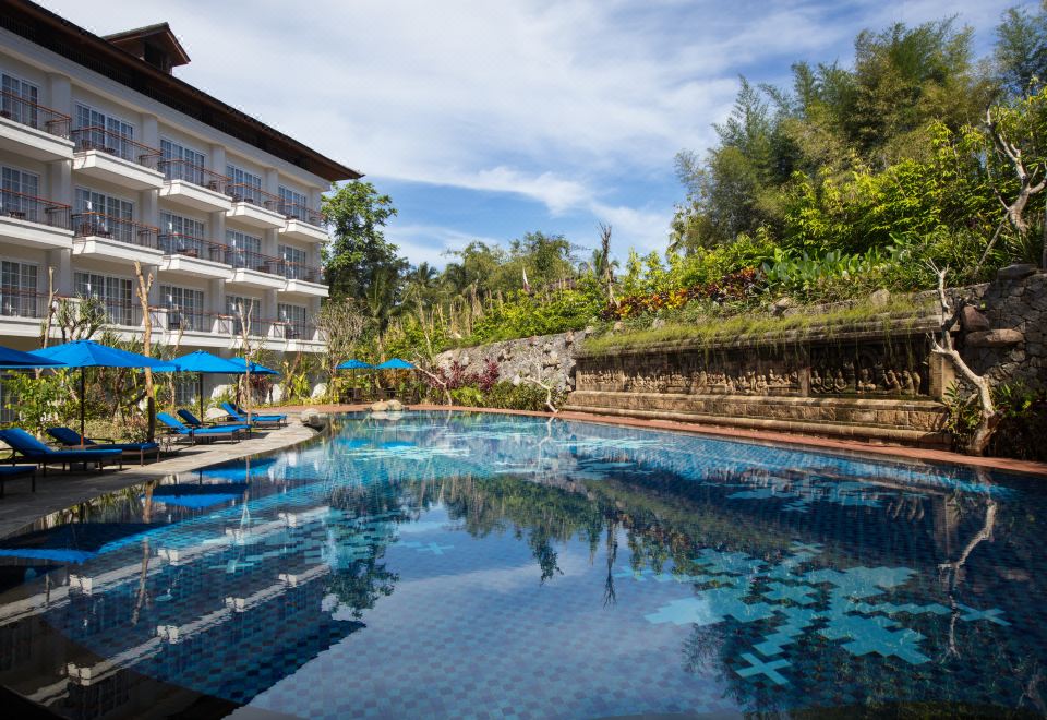 a large swimming pool is surrounded by a hotel with a balcony and lounge chairs at Plataran Heritage Borobudur Hotel