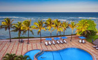 a beautiful outdoor pool area with palm trees , umbrellas , and lounge chairs near the ocean at Sea Cliff Hotel