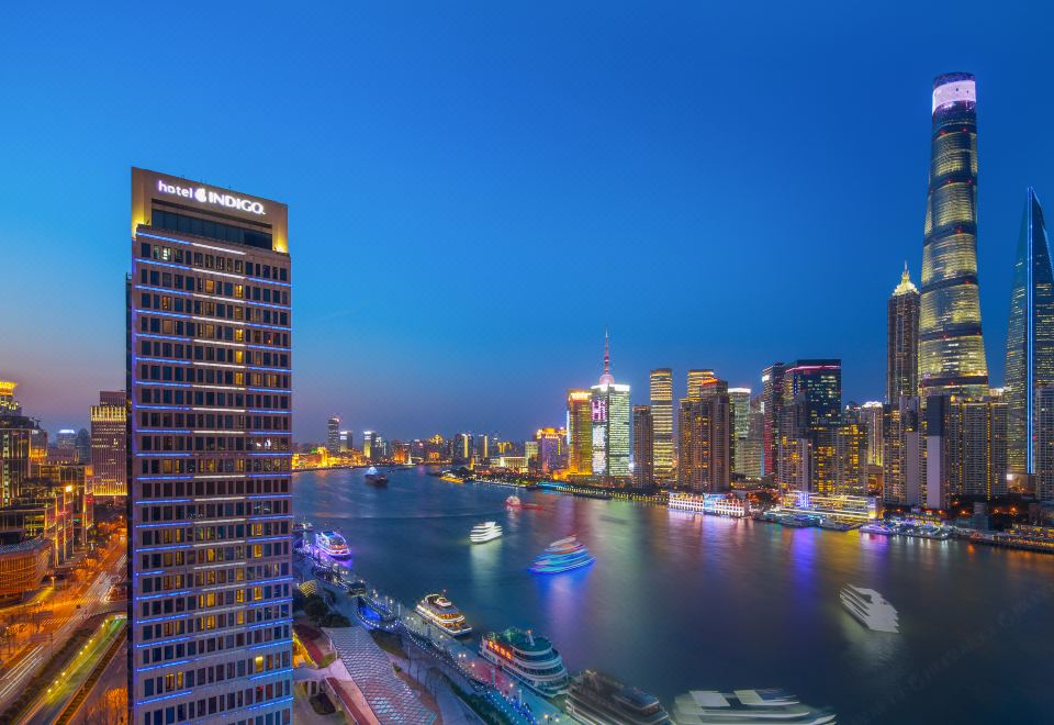 At night, the illuminated city skyline and boats in the foreground create a captivating view from the top floor at Hotel Indigo Shanghai on The Bund