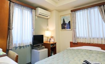 A spacious bedroom with a large bed and a small desk positioned in front of the window is located on the top floor at Hotel Tateshina