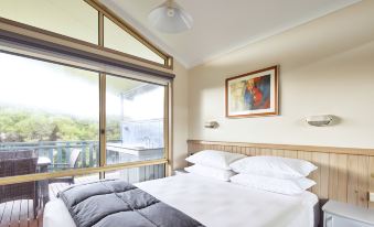 a bedroom with a large bed and a window overlooking a balcony , creating a serene atmosphere at NRMA Merimbula Beach Holiday Resort