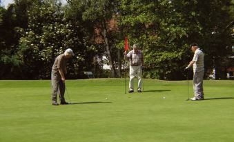 a group of men playing golf on a green field , with one man standing near the hole at Coulsdon Manor Hotel and Golf Club