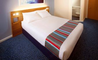 a neatly made bed with a blue and white striped blanket is in a hotel room at Travelodge Porthmadog