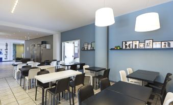 a modern , open - concept cafe with blue walls and white tables , including a few black chairs at B&B Hotel Bologna