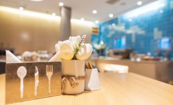 There is an empty place setting on the table with a small white vase containing flowers at Pebble Hotel (Shanghai New International Expo Center Longyang Road Metro Station)