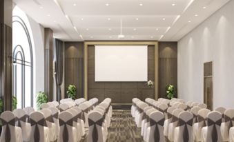 A large conference room is arranged for an event, featuring white chairs and long rectangular tables facing each other at Grand Tourane Nha Trang Hotel