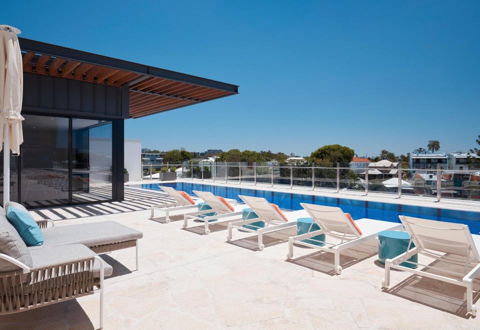 a rooftop pool surrounded by lounge chairs and a bar , with the sun shining brightly overhead at The Cullen Melbourne - Art Series