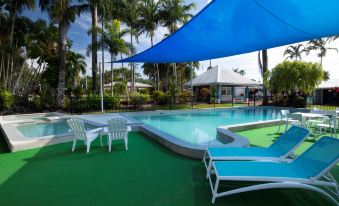 a large swimming pool with a blue umbrella and white lounge chairs surrounded by palm trees at Mission Beach Resort