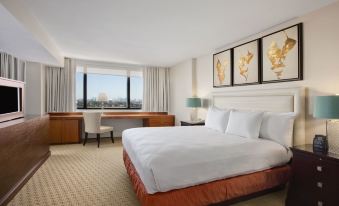 a large bed with white linens and an orange skirt is in a room with a desk , chair , and window at Hilton Miami Airport Blue Lagoon