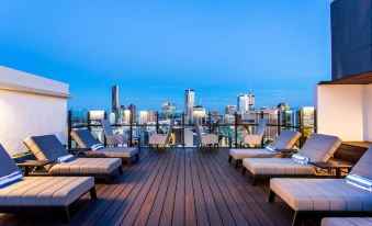a rooftop lounge area with wooden decking , lounge chairs , and a view of the city skyline at Hotel Grand Chancellor Brisbane