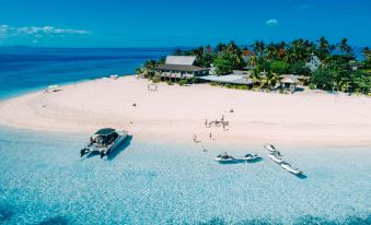 aerial view of a sandy beach with boats docked on the shore , surrounded by palm trees at Beachcomber Island Resort