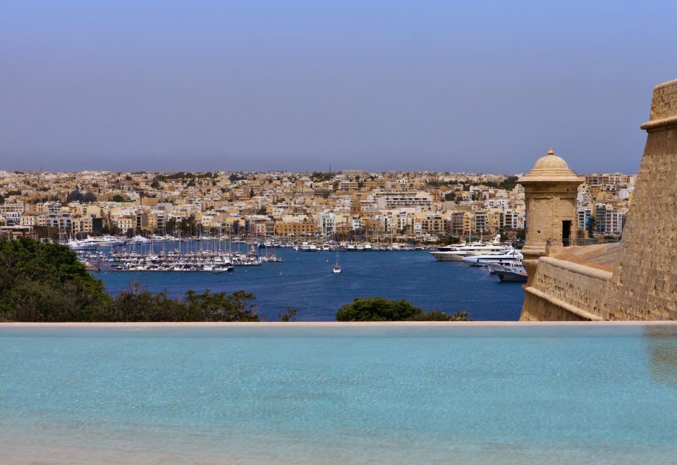 a large pool overlooks a city with tall buildings and boats in the water below at The Phoenicia Malta