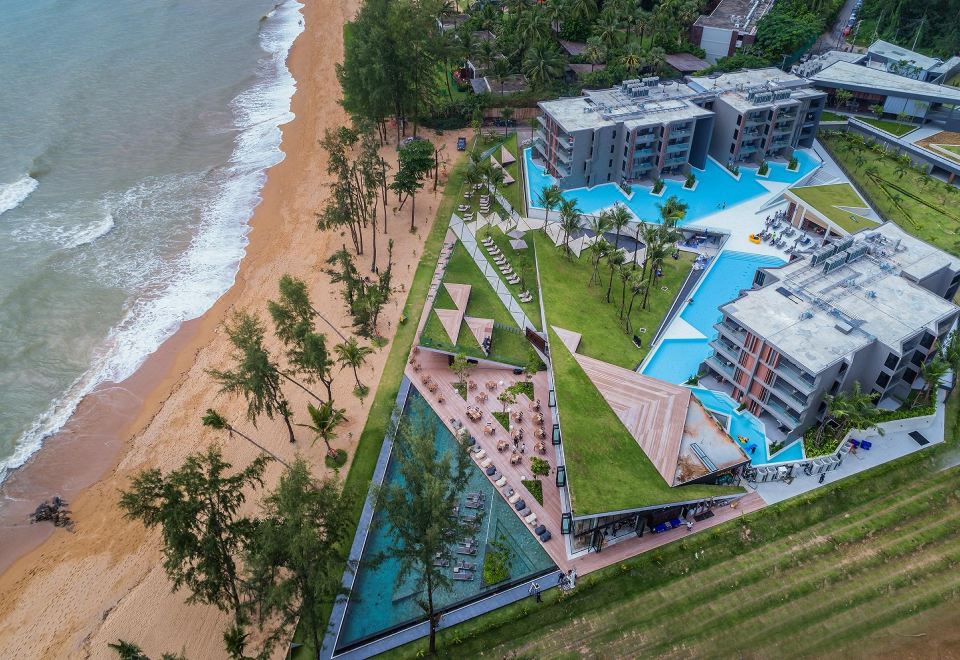 a bird 's eye view of a beachfront resort with multiple buildings , pools , and palm trees at La Vela Khao Lak