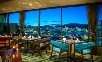 a dining area with tables and chairs , a view of the city through large windows at Copthorne Hotel Wellington, Oriental Bay