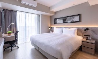 a large bed with white linens is in a room with wooden floors and a window at Oakwood Suites Yokohama