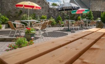 a patio with wooden benches , tables , and chairs , as well as umbrellas to provide shade at The Commercial Hotel