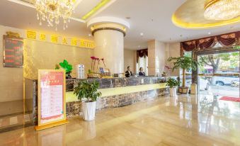 a modern hotel reception area with marble floors , large windows , and potted plants , as well as customers checking in at the counter at Dynasty Hotel