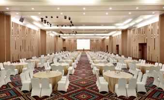 a large conference room with rows of tables and chairs , a screen at the end , and a carpet design on the floor at Aston Kupang Hotel & Convention Center