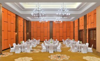 a large , empty banquet hall with orange walls and wooden paneling , decorated with white tables and chairs at Sheraton Kosgoda Turtle Beach Resort