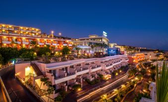 a nighttime view of a modern building with many lights and a blue sign on top at Landmar Costa Los Gigantes