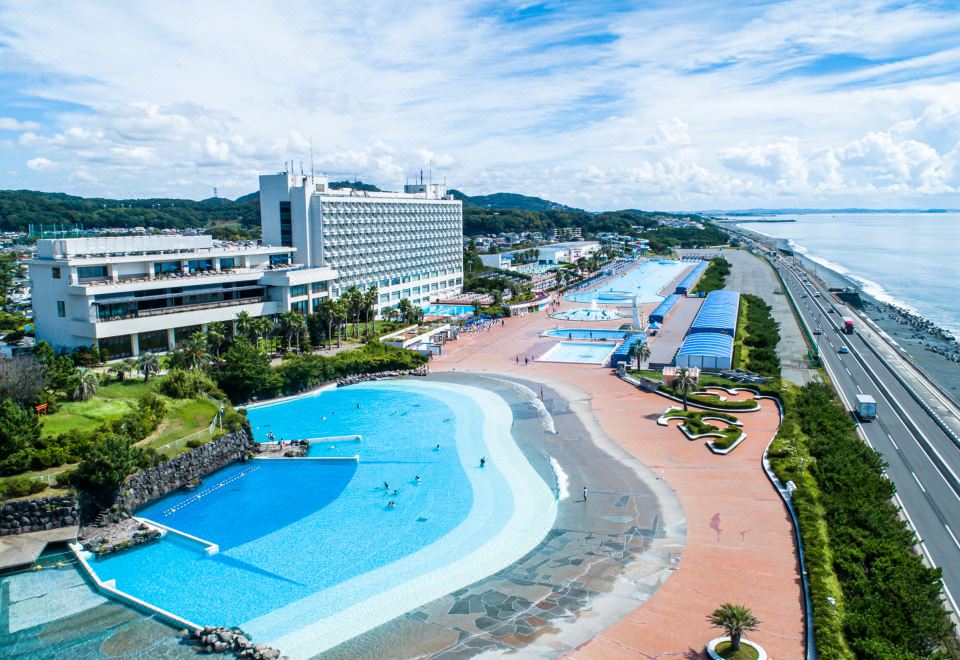 aerial view of a large hotel with a swimming pool surrounded by lush greenery , near the beach at Oiso Prince Hotel
