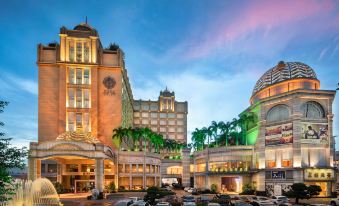 a bustling city square with tall buildings , a fountain in the center , and palm trees lining the street at Golden Hotel