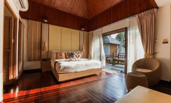 a bedroom with a wooden floor and ceiling , a large bed , and a sliding glass door leading to an outdoor area at Kacha Resort & Spa, Koh Chang