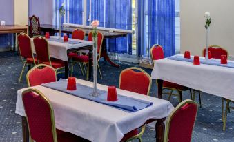 a conference room with red chairs and white tables , each table has a blue tablecloth and red napkins at Empire Hotel