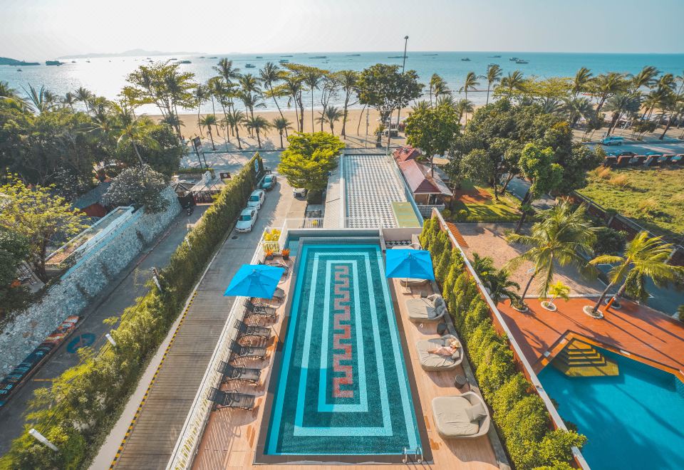 An aerial view showcases a pool and beach at a resort or hotel against a backdrop of clear blue skies at Mera Mare Pattaya