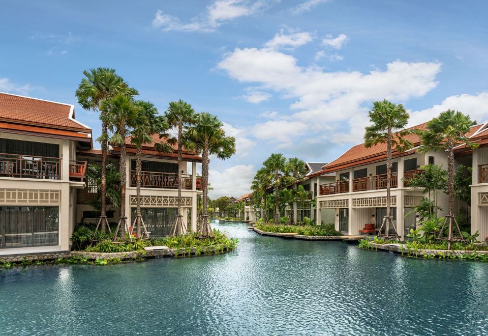 a beautiful resort with multiple buildings , surrounded by lush greenery and a canal , under a blue sky dotted with clouds at Grand Mercure Khao Lak Bangsak