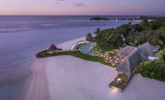 a serene beach scene at dusk , with a group of people gathered around a dining table on the sand at Four Seasons Resort Maldives at Kuda Huraa