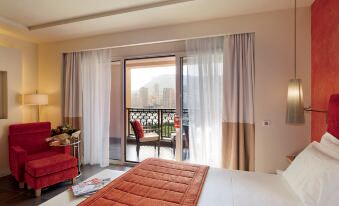 a bedroom with a large bed and red comforter , white curtains , and sliding glass doors leading to a balcony at Monte-Carlo Bay Hotel & Resort
