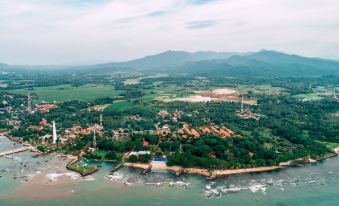 aerial view of a small village by the water , surrounded by lush greenery and mountains in the background at Mambruk Hotel & Convention