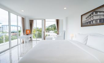 The bedroom features a white bed, large windows, and a door leading to a balcony with views of other areas at B2 Phuket Premier Hotel