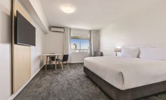 a modern hotel room with a large bed , white walls , and a view of the city through the window at Travelodge Resort Darwin