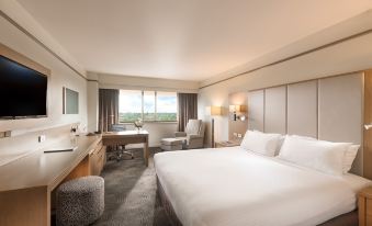 a large , well - lit hotel room with a white bed , desk , and windows offering views of the city at Stamford Plaza Adelaide