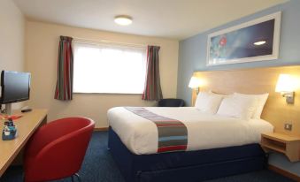 a hotel room with a blue bed , red chairs , and a window with curtains , along with other furniture at Travelodge London Chessington Tolworth