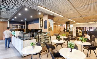 a modern cafe with white tables and chairs , an open kitchen , and a staircase leading to the upper level at Arrow on Swanston
