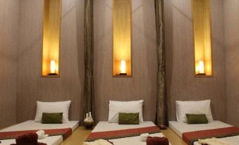 a dimly lit room with three beds , each made up with white sheets and red blankets , surrounded by wooden walls and lit by hanging lamps at Phrae Nakara Hotel
