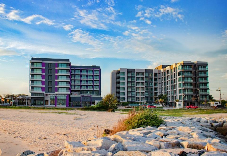 a beach with a row of colorful apartment buildings and a group of people walking on the sand at Fortune Saeng Chan Beach Hotel Rayong