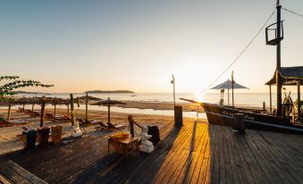 A wooden dock with chairs and tables is situated on the beach, providing a picturesque spot to enjoy the sunset at Aureum Palace Hotel & Resort Ngapali
