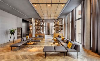 a modern living room with wooden floors , large windows , and a mix of gray and brown furniture at HYPERION Hotel Leipzig