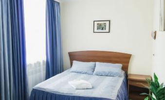 a neatly made bed with blue sheets and pillows , surrounded by a wooden headboard and a window with blue curtains at Avantage