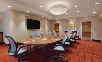 a conference room with a large wooden table surrounded by chairs and a television mounted on the wall at Hilton Garden Inn Falls Church